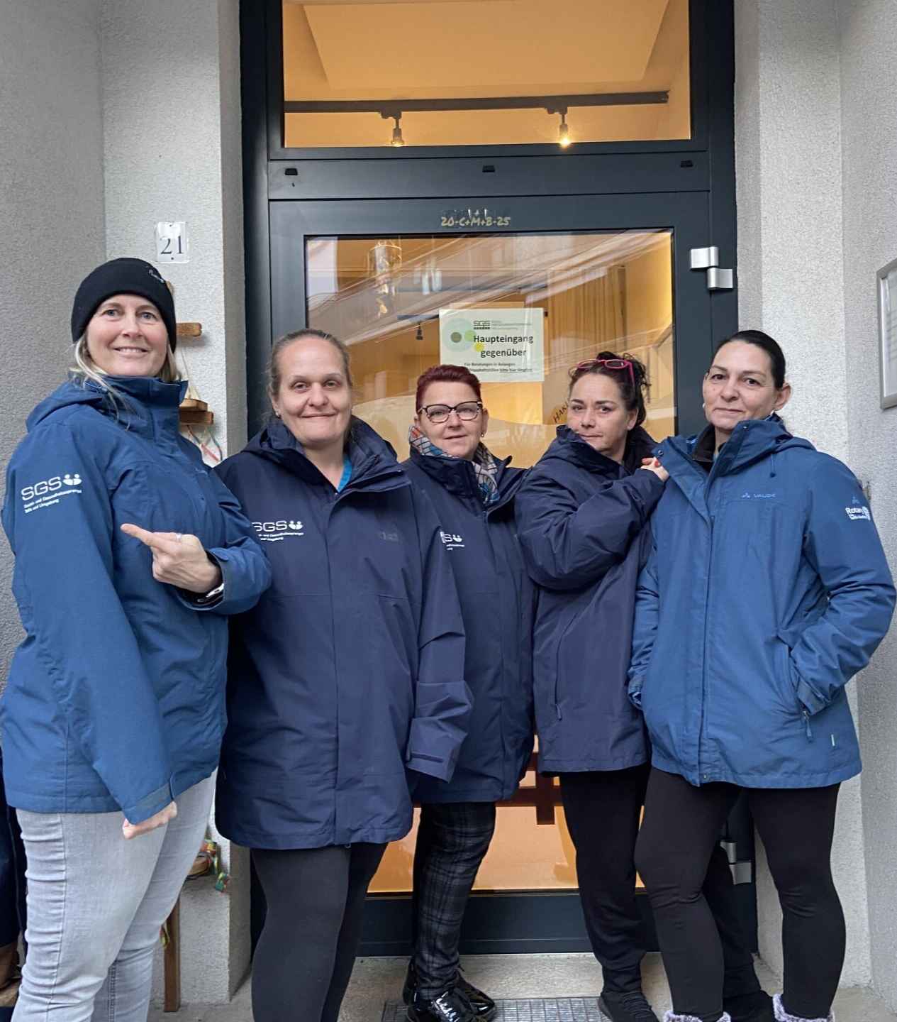 Fünf Mitarbeiterinnen des SGS Telfs stehen im Team vor dem Eingang und tragen blaue Jacken mit Logo – gemeinsamer Einsatz für mobile Pflege.