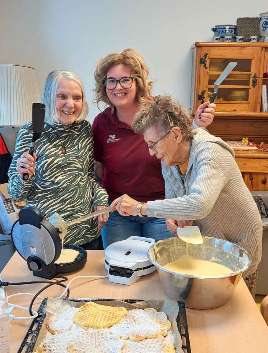 Zwei Seniorinnen backen gemeinsam mit einer SGS-Mitarbeiterin Waffeln – fröhliche Stimmung bei einer gemeinsamen Aktivität im Tageszentrum.
